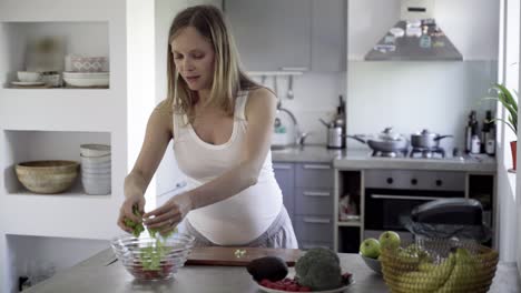Friedliche-Zukünftige-Mutter,-Die-Salat-Auf-Dem-Küchentisch-Schneidet